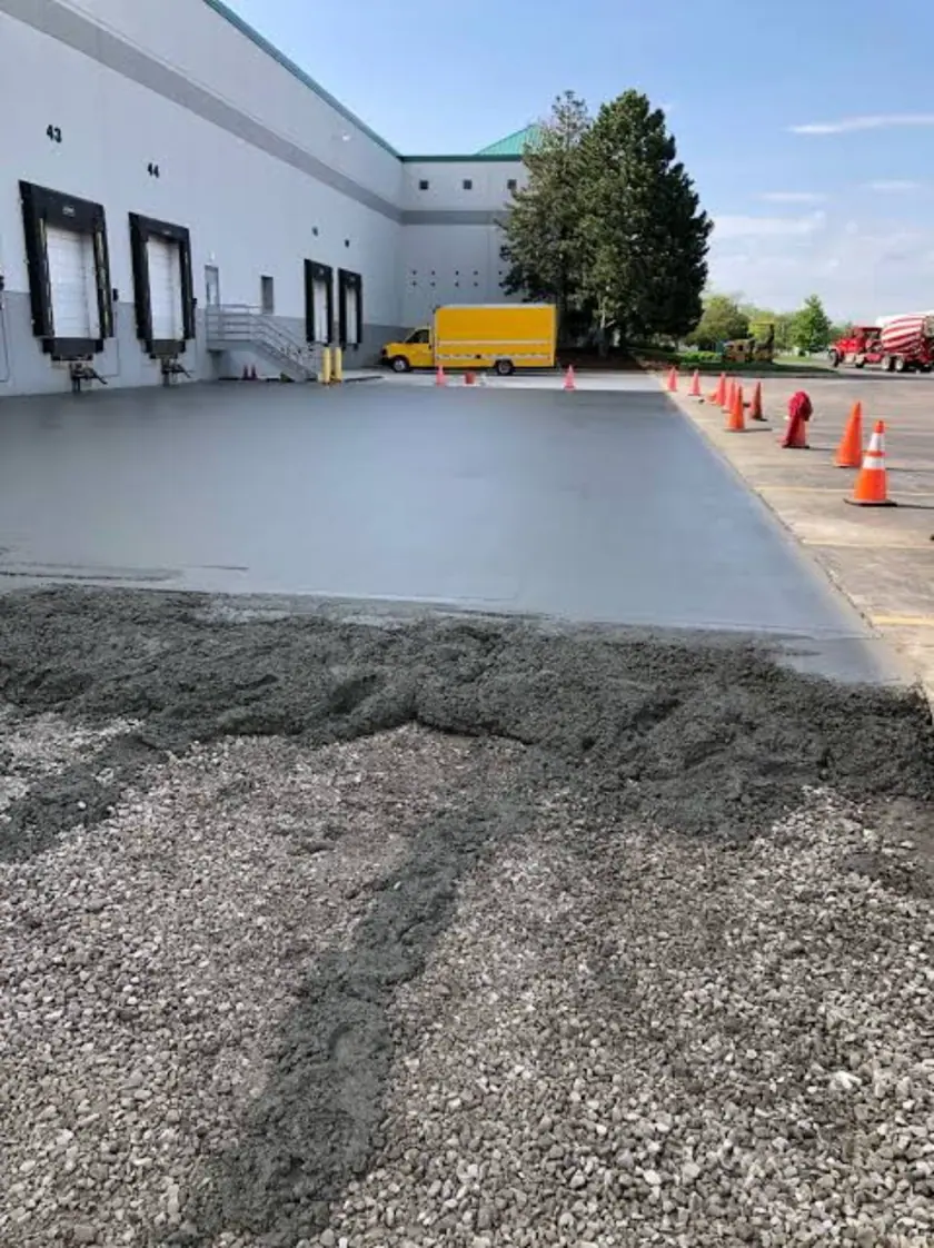 Freshly placed concrete loading-dock apron outside an industrial warehouse, marked off by orange traffic cones